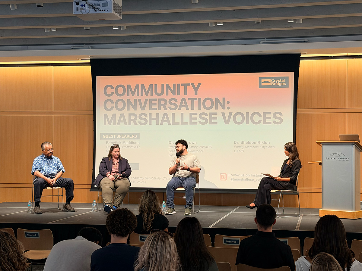 The panel seated on stage beneath the Community Conversation title slide.